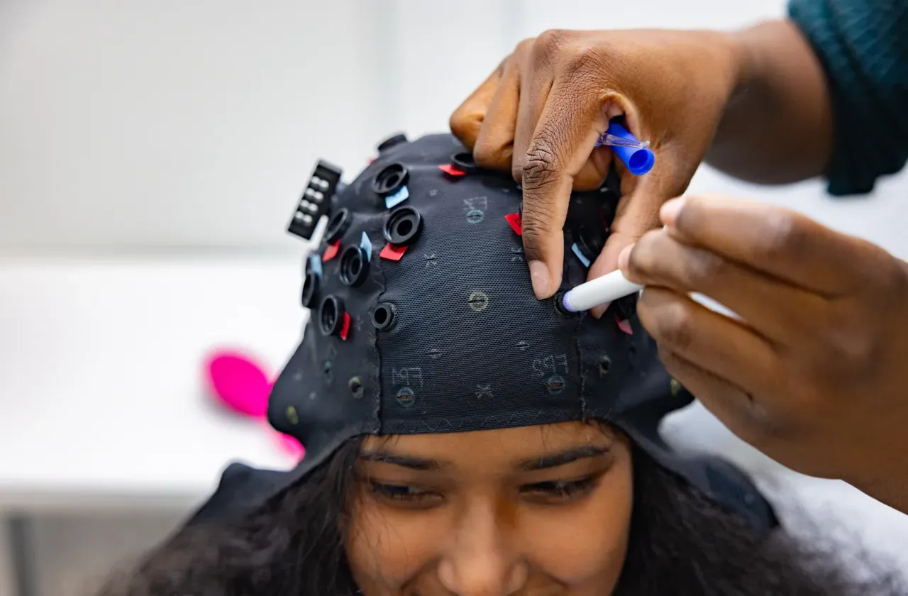 Student researcher Kris Cheaye fits an fNIRS cap to Gloriamar Esteves’s head